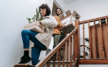 couple carrying moving boxes and plants down the stairs