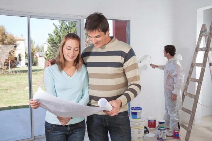 couple looking at plans of their new house and man painting behind